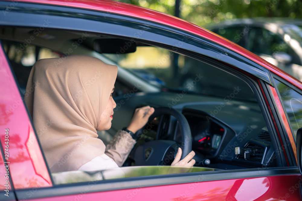 Portrait of young Asian Muslim woman driver, happy woman driving a red car, copy space. ride sharing, trip, long journey concept. Portrait of young Asian Muslim woman driver, happy woman driving a red car, copy space. ride sharing, trip, long journey concept.