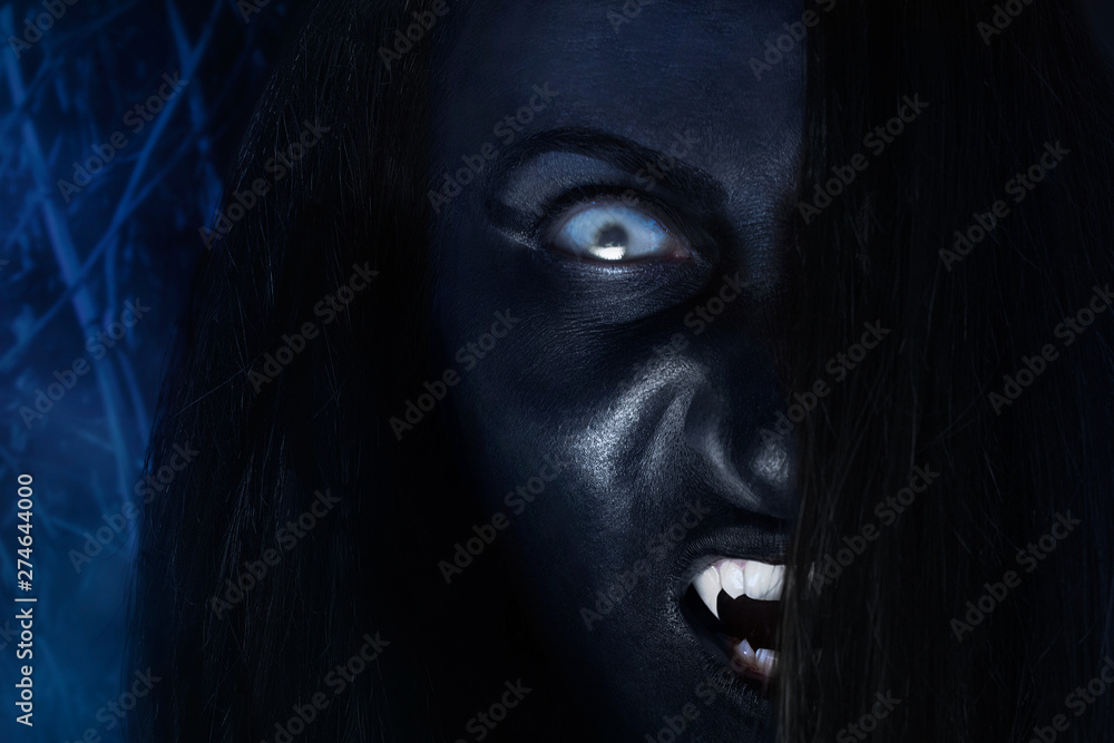 Creepy dark vampire face with white eyes and fangs on night wood background. Creepy dark vampire face with white eyes and fangs on night wood background.