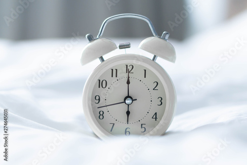 Alarm clock on white bad with light from window, selective focus