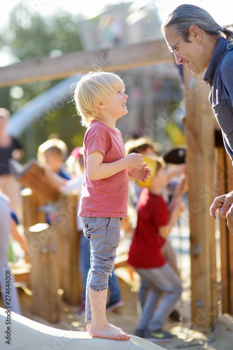 Little boy having fun with his grandfather on outdoor playground of public park at sunny summer day.