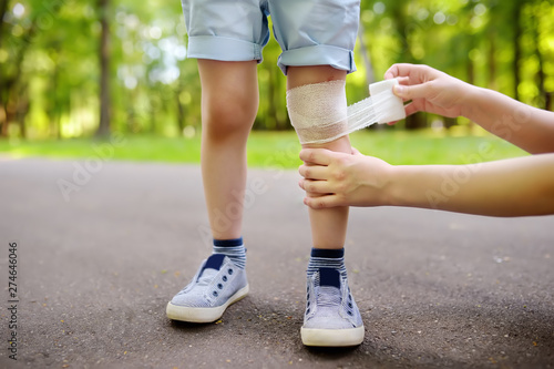 Mother hands applying antibacterial medical bandage on child's knee after falling down.