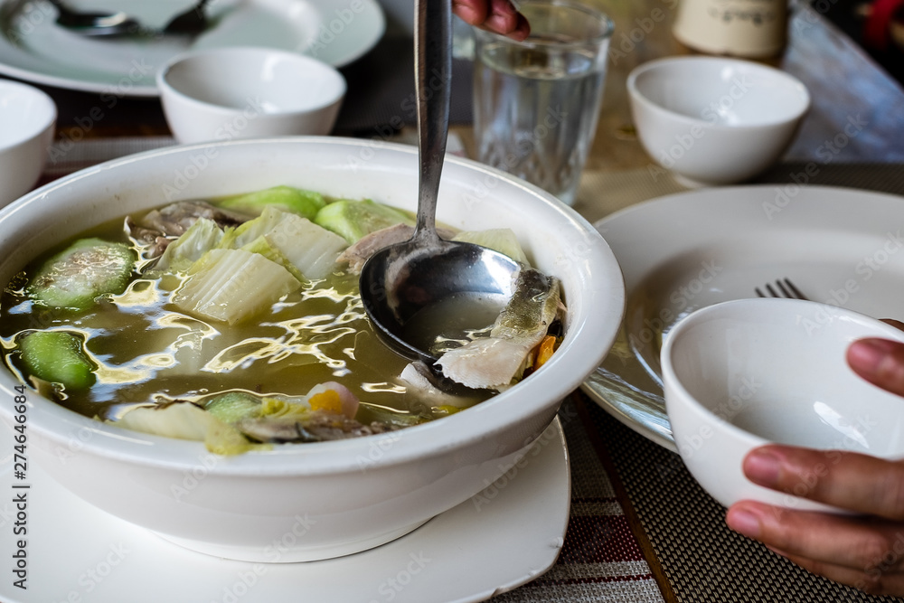 Woman's hand and scooping slice of Pompano fish soup into a small bowl. Pompano fish or Jack also known as Pampano for Filipinos or Trachinotus blochii. Woman's hand and scooping slice of Pompano fish soup into a small bowl. Pompano fish or Jack also known as Pampano for Filipinos or Trachinotus blochii.