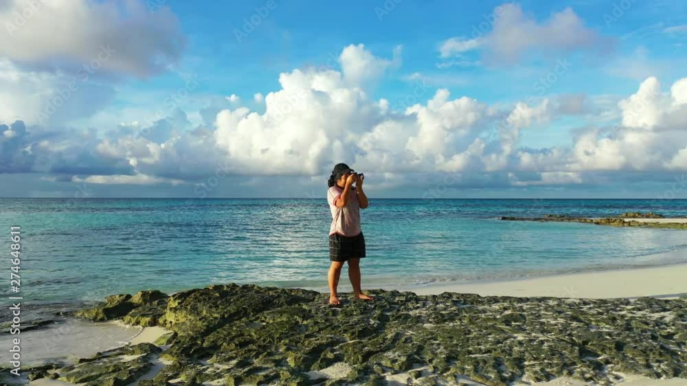 Young girl taking pictures with her camera in a small rocky beach in Thailand. Turquoise waters behind her Young girl taking pictures with her camera in a small rocky beach in Thailand. Turquoise waters behind her