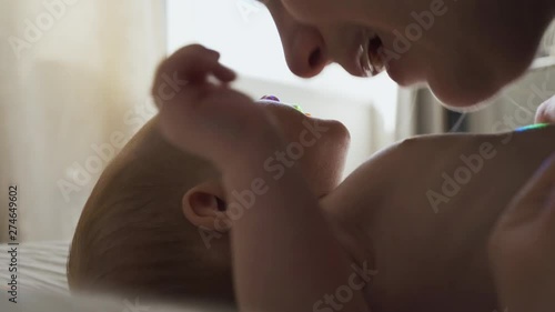 Close up, low angle view of mum loving her newborn baby. Mommy playing with son by rubbing her nose on his lips. Baby wiggles happily as he plays with mom.