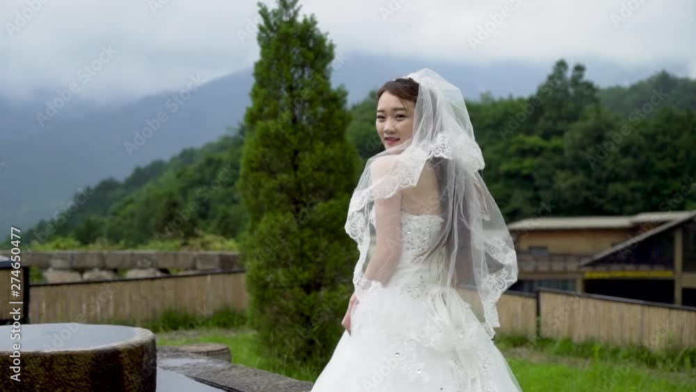 Slow motion shot of a beautiful Chinese woman in a wedding dress standing outside and looking over her shoulder at the panning camera. Slow motion shot of a beautiful Chinese woman in a wedding dress standing outside and looking over her shoulder at the panning camera.