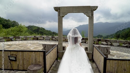 In slow motion, a bride walks down the aisle and through the treshold before the camera moves past her towards the misty landscape. photo