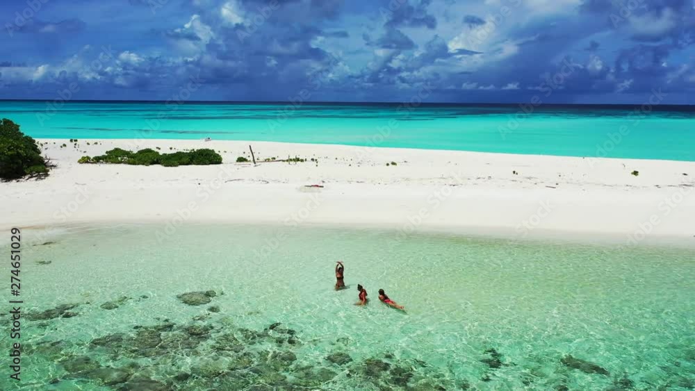 Three young women in shallow turquoise water in front of a sandbank. Dramatic Sky above the Caribbean. Dolly in, aerial Three young women in shallow turquoise water in front of a sandbank. Dramatic Sky above the Caribbean. Dolly in, aerial