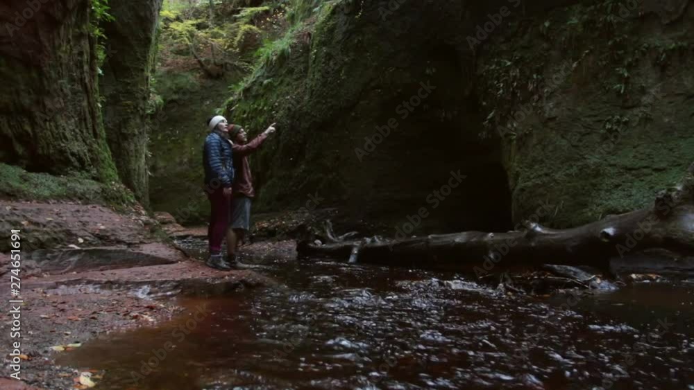 Man and woman look a beautiful gorge with creek flowing beside them in Scotland United kingdom, pointing at something spectacular Man and woman look a beautiful gorge with creek flowing beside them in Scotland United kingdom, pointing at something spectacular