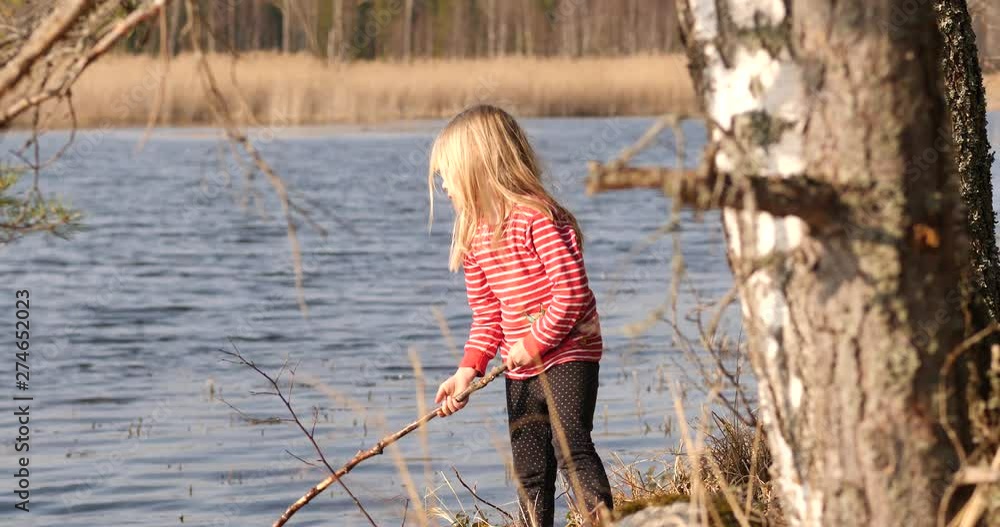 Girl playing alone with big stick by the water the old-fashion way, calm active childhood, contrast to video games