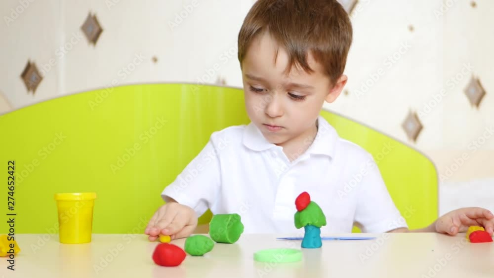 A child sitting at the table, plays in colorful sculptures of plasticine or dough for games A child sitting at the table, plays in colorful sculptures of plasticine or dough for games