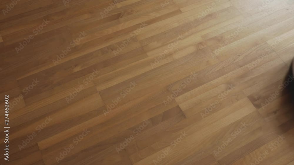 A white golden vacuum cleaner robot drives from left to right through the frame whilst cleaning a laminate floor A white golden vacuum cleaner robot drives from left to right through the frame whilst cleaning a laminate floor