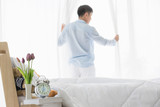 Asian man parts the curtain in bedroom..