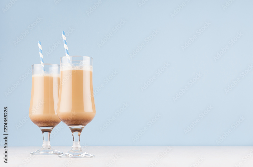 Refreshment coffee drinks with cream, foam and striped straw in wineglass in light blue interior on white wooden table, copy space. - obrazy, fototapety, plakaty 