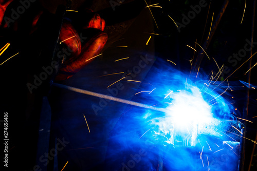 Fototapeta Naklejka Na Ścianę i Meble -  Welder worker performs jump welding. Man welder in protective gloves performs arc-welding process of metal structures. Flying sparks from the welding machine. Background construction site
