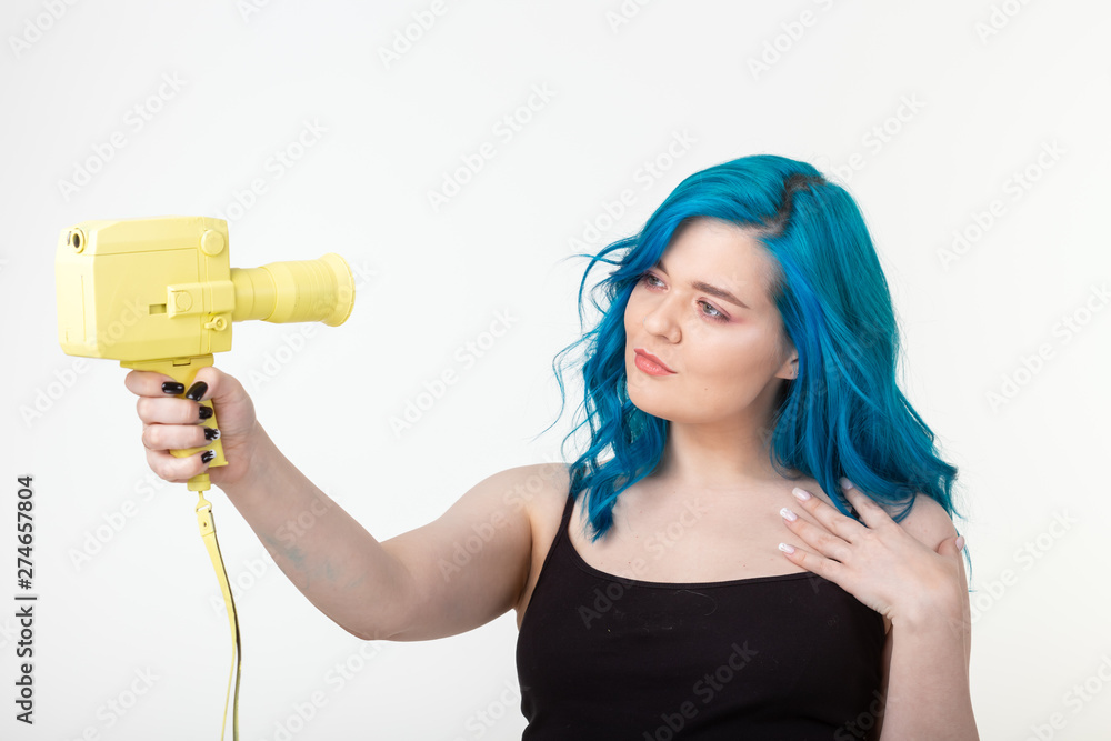 People, hobby and fashion concept - Beautiful girl with blue hair hold yellow retro camera on white background People, hobby and fashion concept - Beautiful girl with blue hair hold yellow retro camera on white background