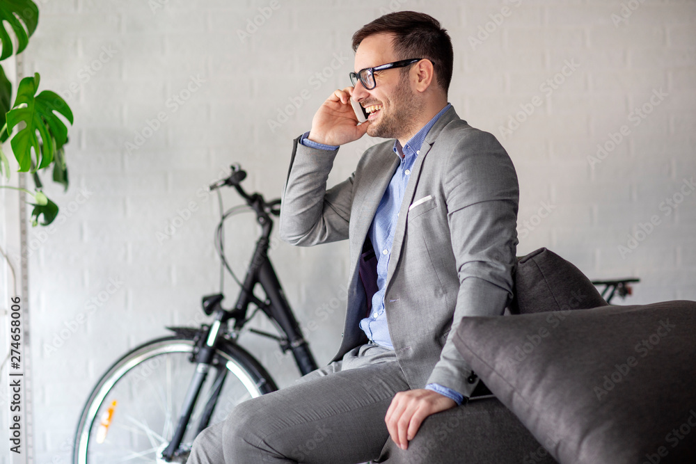 Man with bike on background sitting at the end of sofa and talking on mobile phone Man with bike on background sitting at the end of sofa and talking on mobile phone