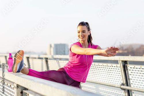 Woman exercise and stretch before jogging on the bridge and listen music. Bottle of the water standing on the fence