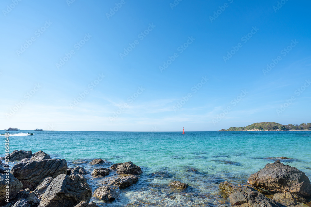 Landscape wide shot selective focus of rocky sand beach at tropical island in summer. Red buoy floating in blue sea with sky and clouds backgrounds. The sun glimmering sunlight peeking the sea surface
