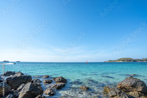 Landscape wide shot selective focus of rocky sand beach at tropical island in summer. Red buoy floating in blue sea with sky and clouds backgrounds. The sun glimmering sunlight peeking the sea surface