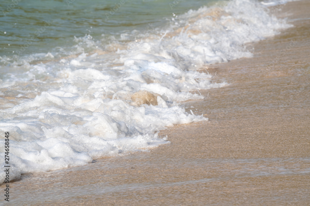 Selective focus of soft ocean sea wave splashing the tropical island beach making soft white bubble foam.The sun glimmering sunlight peeking the sea surface in hot summer holiday vacation travel trip.