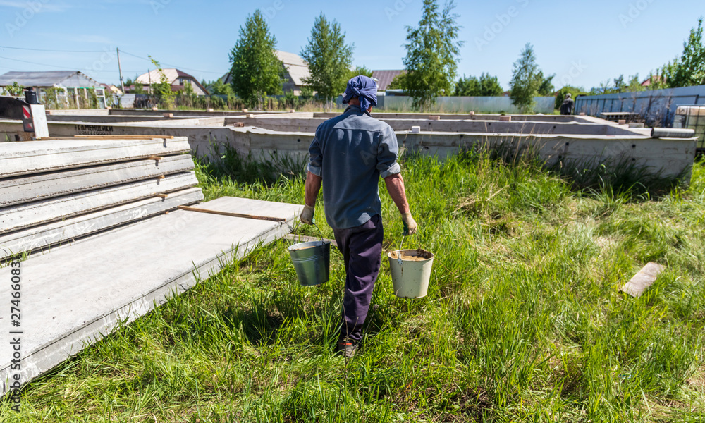 Worker with buckets of concrete at a house construction