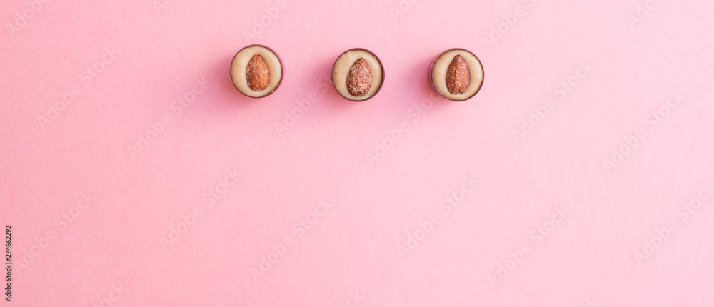 Round chocolates with pistachio cream and salted almonds on pink background. Flat lay and copy space Round chocolates with pistachio cream and salted almonds on pink background. Flat lay and copy space