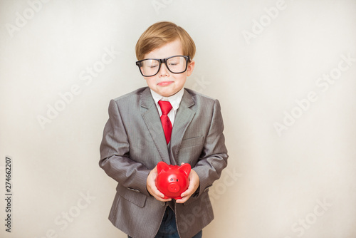Upset child boy stands in a fashionable suit with a piggy Bank in his hands. Success, creative and innovation business concept © irena_geo