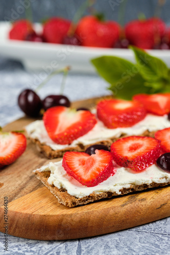 bread with cottage cheese, fresh strawberries and cherries on a wooden Board, on a gray background, selective focus