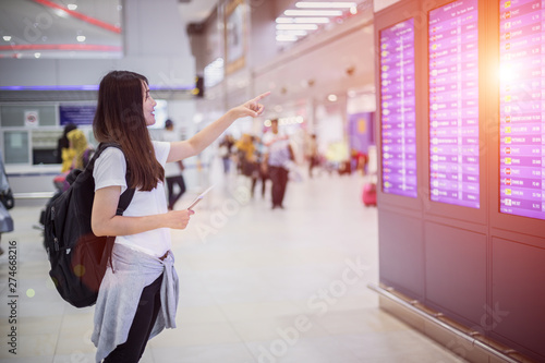 Travel Concept , Young woman tourists with backpack and hand passport in international airport terminal, looking at information board.
