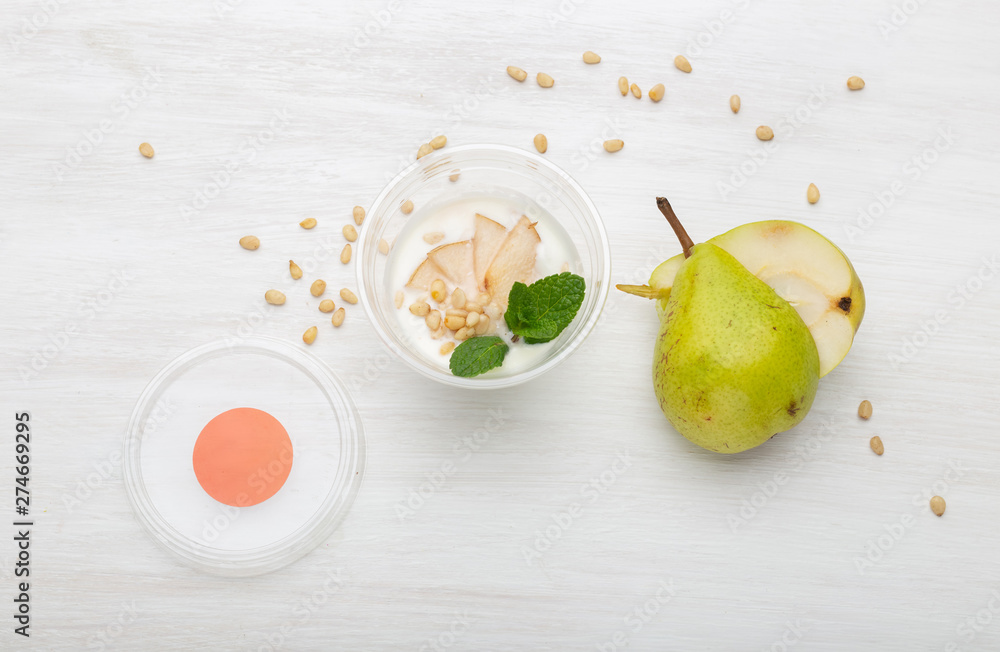 Yogurt pear slices and mint and pine nuts lie in a lunch box on a white table next to scattered with pine nuts and pear slices. Healthy eating concept. Yogurt pear slices and mint and pine nuts lie in a lunch box on a white table next to scattered with pine nuts and pear slices. Healthy eating concept.