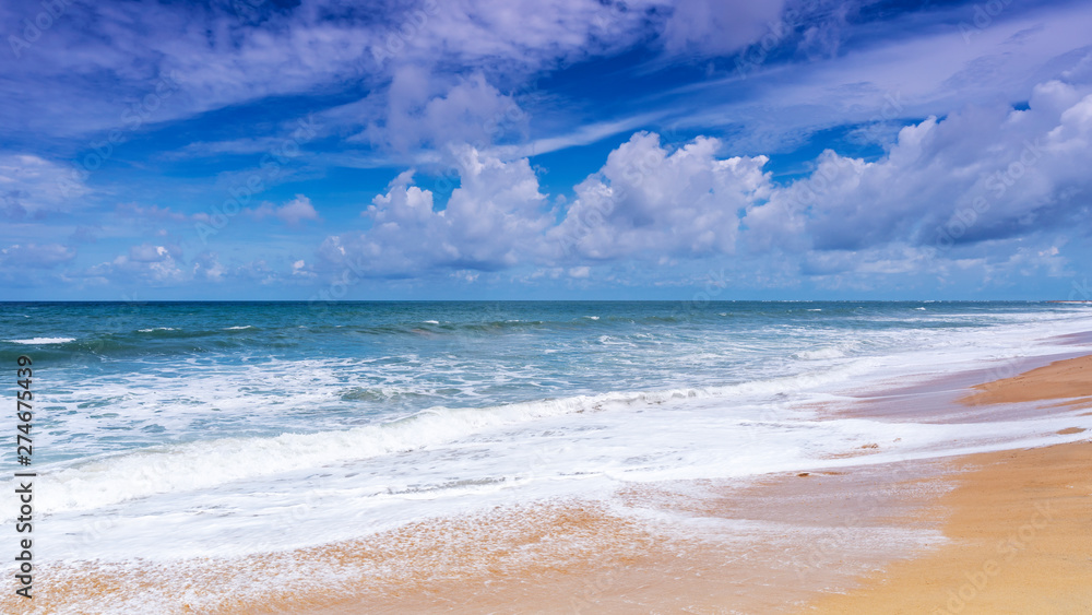 Beautiful Tropical sandy beach with blue ocean and blue sky background and wave crashing on sandy shore