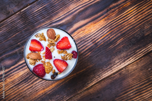 Health concept - Top view bowl of homemade granola with yogurt and fresh strawberries on wooden background.