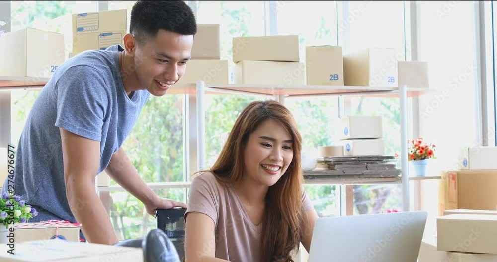 Young Asian couple in product store, woman using notebook computer for checking stock, their happy with their business. Young Asian couple in product store, woman using notebook computer for checking stock, their happy with their business.