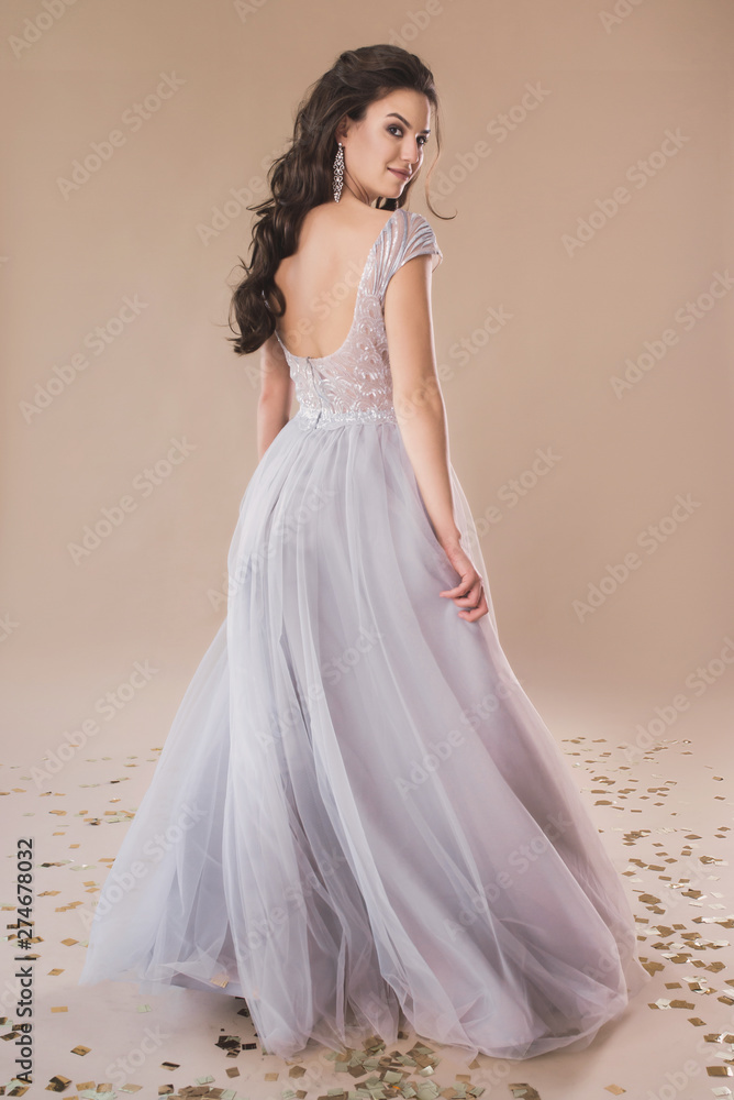Fototapeta premium Piękna dziewczyna w eleganckiej sukni wieczorowej pozowanie na portret pełnej długości beżowym tle papieru