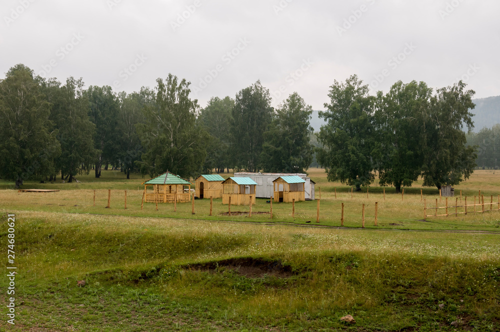 Obraz premium Heavy clouds in the cold autumn sky over village with small light wooden houses far away in the mountains. Wide river flows near with reflections in the water. Travelling on the suburb roads. Fog