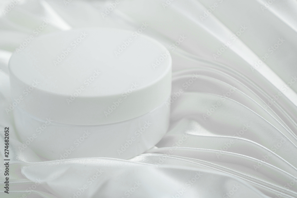 Jar of cosmetic product on white background. Cream white jar is on the tender white fabric folds background. Mockup of cosmetic jar on the gathers of satin fabric backdrop for spa salon. Copyspace Jar of cosmetic product on white background. Cream white jar is on the tender white fabric folds background. Mockup of cosmetic jar on the gathers of satin fabric backdrop for spa salon. Copyspace