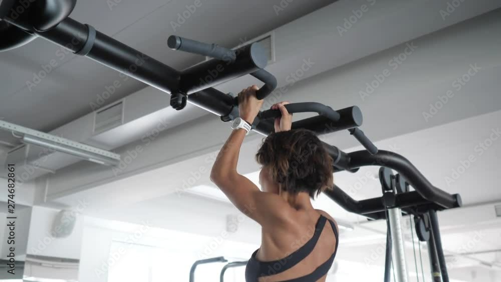 Portrait of slim sporty woman is doing pull-ups on horizontal bar with a narrow grip in gym. Mature woman in sportswear, side view. Portrait of slim sporty woman is doing pull-ups on horizontal bar with a narrow grip in gym. Mature woman in sportswear, side view.
