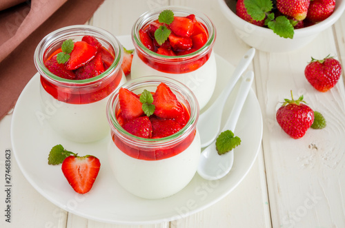 Dietary creamy yogurt panna cotta with fresh strawberry sauce in glass jars.