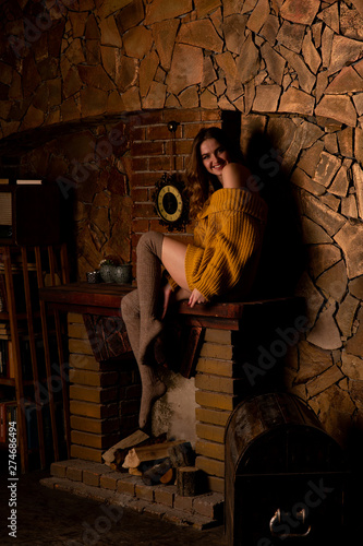 Beautiful girl sitting next to the fireplace. Luxury interior decorated for Christmas with fir branches and toys