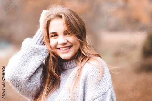 Smiling teen 14-16 year old wearing warm sweater outdoors. Looking at camera. Autumn season. 20s.