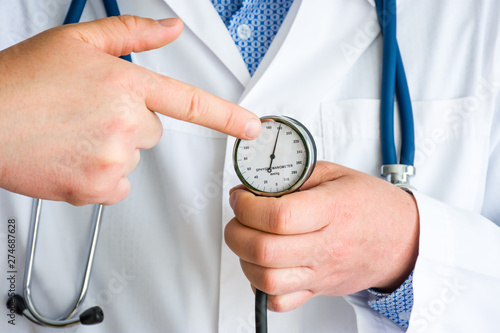 Indication of high blood pressure (hypertension) in patient concept photo. Doctor with stethoscope pointing by finger at level of high blood pressure in patient on scale of mechanical sphygmomanometer