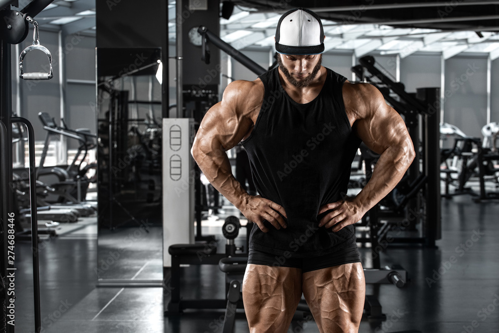 Fototapeta premium Muskularny mężczyzna pokazujący mięśnie w siłowni, trening. Silny mężczyzna kulturysty