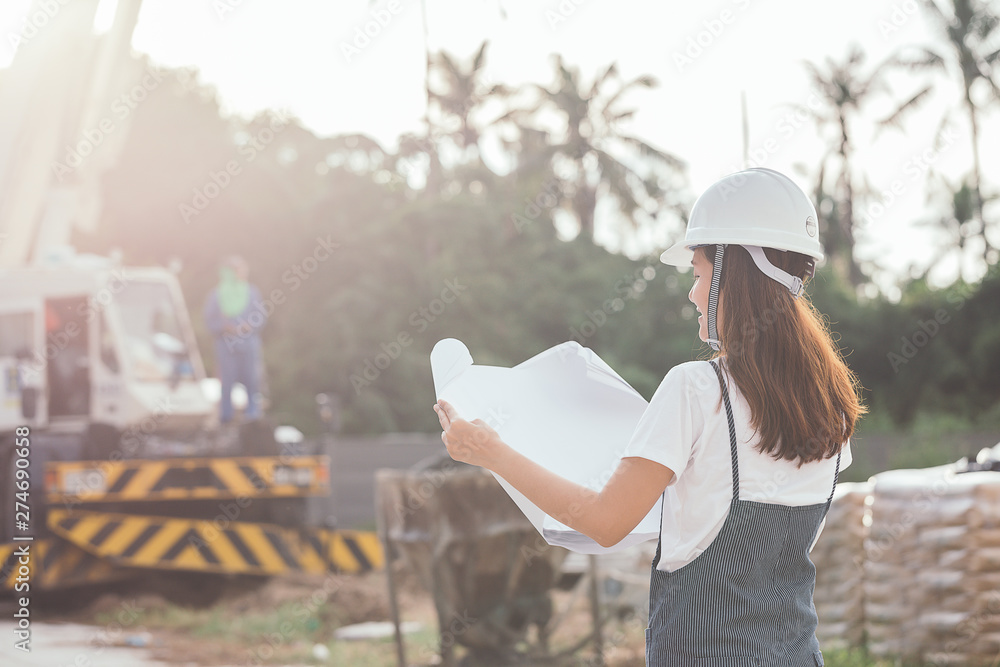 Young woman engineer with a blueprint at an outdoor construction site during a job survey, Engineering and architecture concept - Image