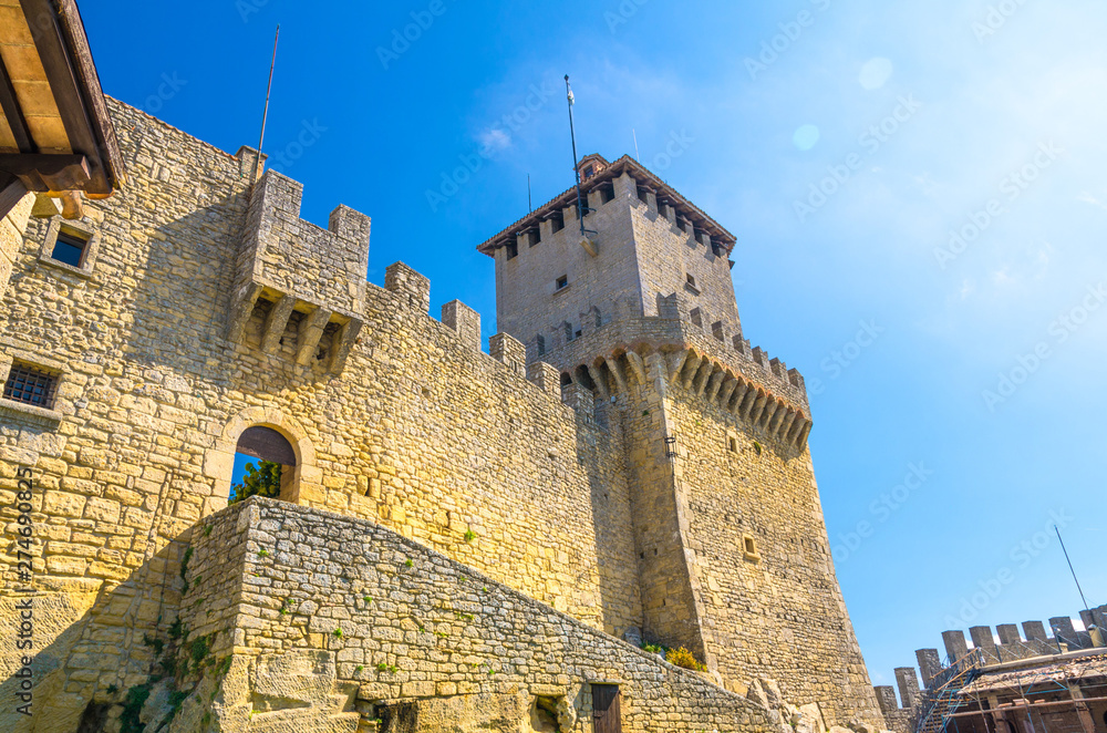 Prima Torre Guaita first medieval tower with stone brick fortress wall with merlons on Mount Titano rock, blue sky white clouds copy space background, Republic San Marino
