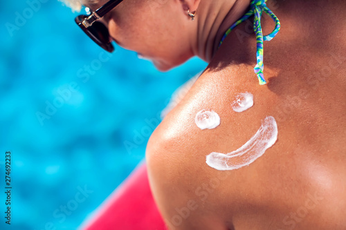 Woman with sun crem on her back in shape of smile. People, summer, vacation and healthcare concept