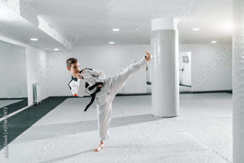 Caucasian boy in dobok kicking in dollyo-chagi pose. Taekwondo training concept.