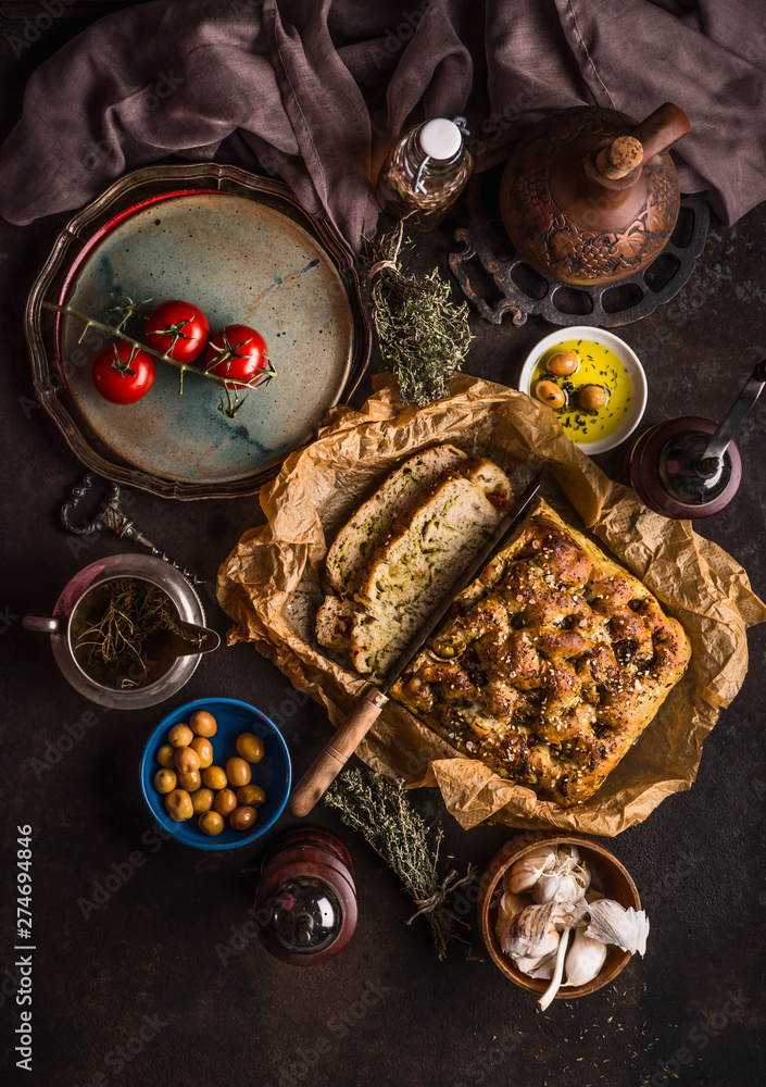 Traditional Italian focaccia bread to lunch, dinner or snack on rustic table with knife olives and olive oil, top view. Italian food concept.