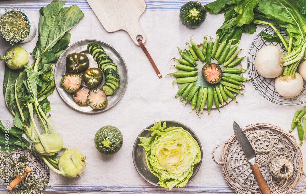 Flat lay green vegetables in bowls on light table with knife: green peas, kohlrabi, lettuce, zucchini, cucumber, green tomatoes. Top view. Clean vegetarian eating and cooking concept. Flat lay green vegetables in bowls on light table with knife: green peas, kohlrabi, lettuce, zucchini, cucumber, green tomatoes. Top view. Clean vegetarian eating and cooking concept.