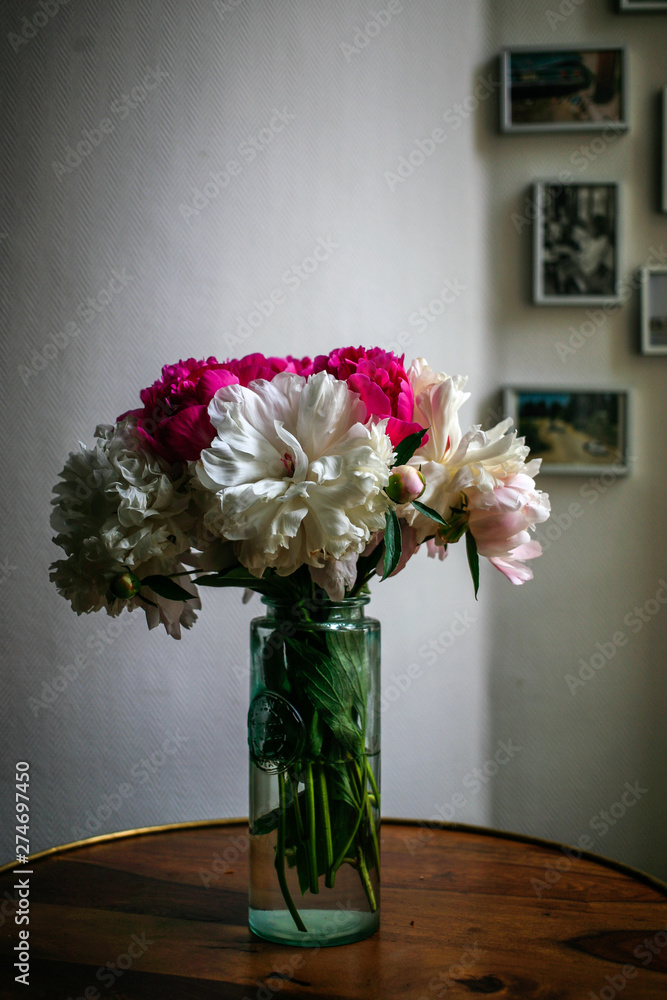 Gorgeous white and pink pions in a glass vase on the table with some light in front of the Parisian window Gorgeous white and pink pions in a glass vase on the table with some light in front of the Parisian window