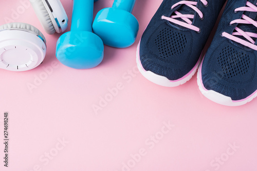 Female sport shoes, blue dumbbells andwhite headphones on a pink background with copy space, top view photo